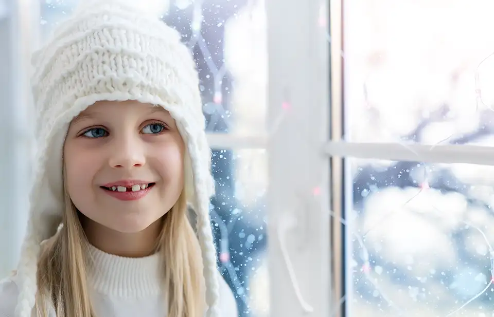 Small girl wearing a warm cap looking out a window into a frosted wonderland.