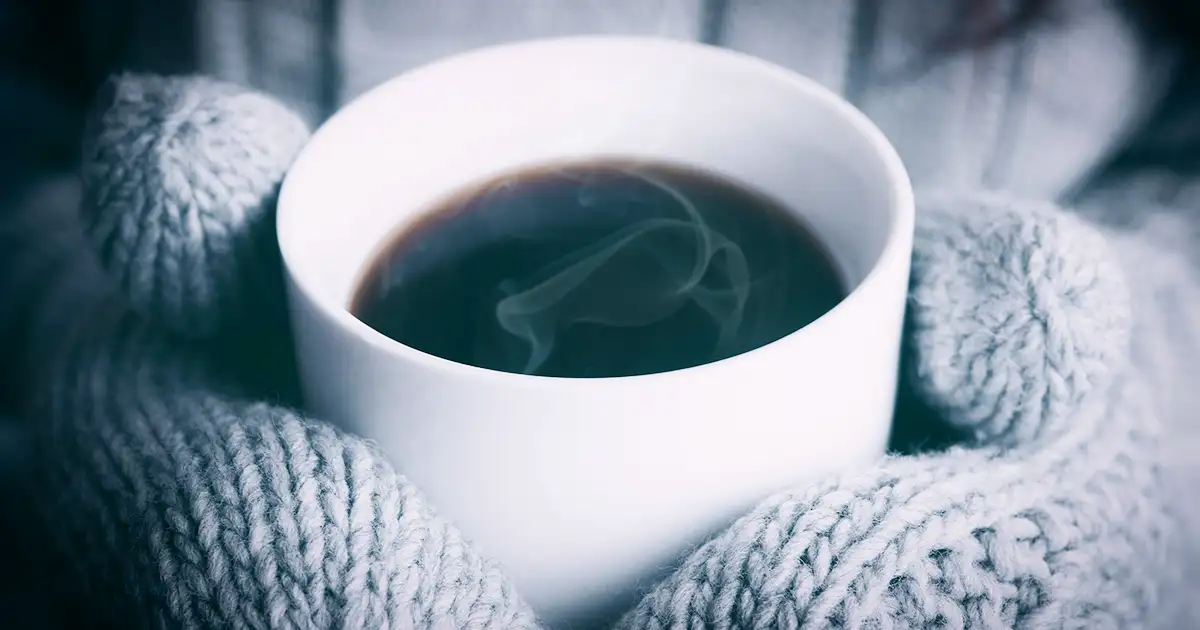 Cold hands inside mittens warm up with a cup of hot coffee